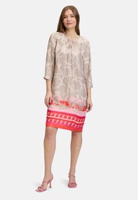 Sukienka w kwiatowy wzór z jasnobeżową górą, intensywnie różowym gradientem u dołu oraz rękawami do łokcia. Połączona z różowymi sandałami na obcasie.