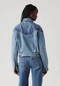 Giubbotto in denim di colore azzurro chiaro con design classico, dotato di colletto, chiusura a bottoni e cuciture a contrasto lungo le spalle.