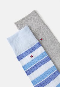 Deux paires de chaussettes : l'une bleu clair avec des rayures bleues et un logo, l'autre grise avec une finition texturée. Les deux sont côtelées en haut.