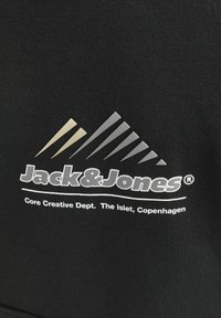 Black fabric featuring the Jack&Jones logo in white. Below, "Core Creative Dept. The Islet, Copenhagen" in smaller text. Mountain graphic design.