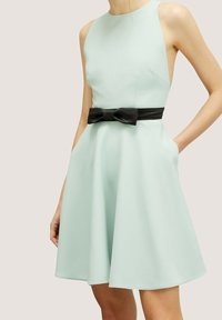 Vaalean mintunvihreä ilman hihoja oleva mekko, jossa on suljettuna vartaloon istuva yläosa ja levenevä hame, jota korostaa musta satiininen vyösolki. Mekossa on sivutaskut.