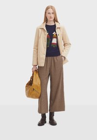 Beige Kord-Jacke, marineblauer Pullover mit Grafik, braune karierte weit geschnittene Hose, braune Ledertasche, schwarze Stiefeletten, glatte Textur.