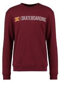 Mörkröd sweatshirt med långa ärmar, rund ringning, ribbad mudd och fåll. Har vit text som står "DC SKATEBOARDING" iögonfallande på framsidan.