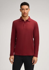 Polo a maniche lunghe color bordeaux con un motivo a diamante testurizzato, dotato di colletto con bottoni e taglio dritto, abbinato a pantaloni scuri.