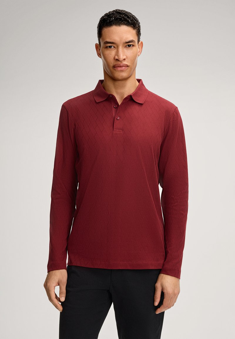 Polo a maniche lunghe color bordeaux con un motivo a diamante testurizzato, dotato di colletto con bottoni e taglio dritto, abbinato a pantaloni scuri.