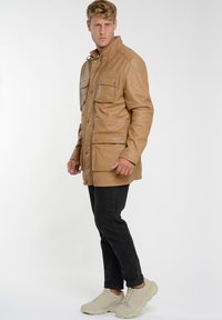 Brun læderjakke med fire frontlommer, trykknaplukning og krave, parret med sorte jeans og lyse sneakers.