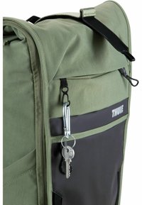 Sac à dos vert et noir en tissu texturé, avec des zips et un mousqueton tenant des clés. Présente un logo Thule en blanc bien visible.