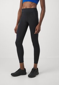 Svarta högmidjade leggings gjorda av elastiskt tyg, med en kroppsnära silhuett och sömdetaljer. Kombinerade med svarta sportskor.