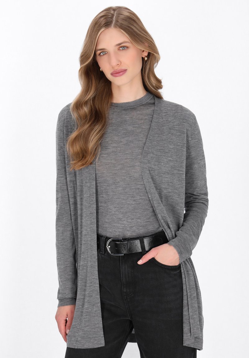 Cardigan grigio a maniche lunghe realizzato in tessuto morbido, design aperto sul davanti, indossato sopra un top grigio, abbinato a pantaloni neri e una cintura nera spessa.