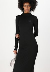 Vestido preto de manga longa com um decote alto e silhueta ajustada, com um design texturado e um logotipo em strass no peito.