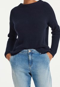 Granatowy sweter o fakturowanym splotie z okrągłym dekoltem i długimi rękawami, zestawiony z jasnoniebieskimi dżinsami z klasycznym zapięciem na guziki.