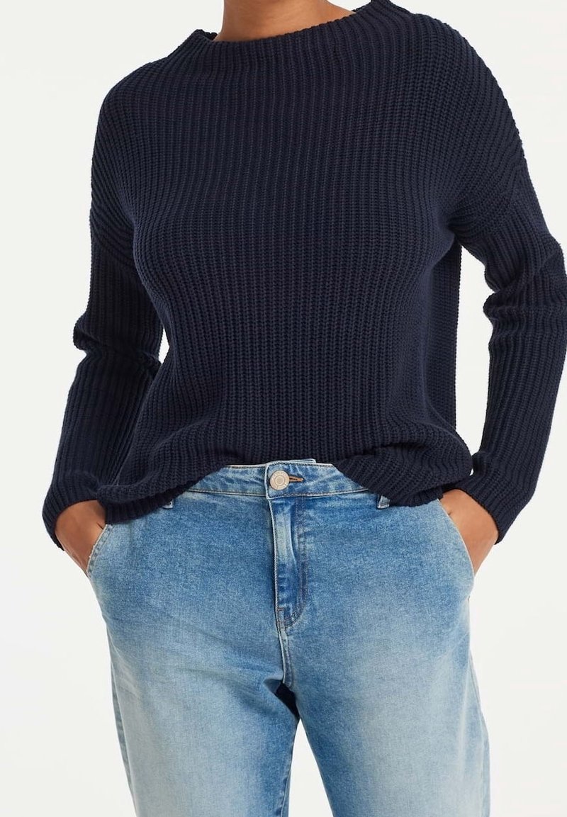 Granatowy sweter o fakturowanym splotie z okrągłym dekoltem i długimi rękawami, zestawiony z jasnoniebieskimi dżinsami z klasycznym zapięciem na guziki.