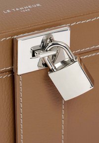 Bolso de cuero marrón con costuras blancas. Presenta un candado y cierre de plata. Nombre de la marca "LE TANNEUR 1898" grabado en la parte superior.