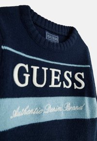 Maglione blu navy con scollatura a girocollo a costine, caratterizzato da strisce orizzontali in azzurro chiaro e bianco. Logo "GUESS" in evidenza in bianco.