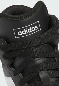 Czarne sneakersy Adidas z gładkiej skórzanej cholewki, grubymi czarnymi sznurówkami i wyściełanym kołnierzem. Posiadają białą naszywkę z logo na języku.