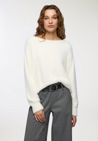 Maglione bianco peloso con scollo ampio, vestibilità rilassata e maniche lunghe. Abbinato a pantaloni a scacchi grigi a vita alta e una cintura nera.