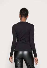 Schwarzer, langärmeliger, enganliegender Oberteil aus elastischem Material, mit Rundhalsausschnitt und nahtlosem Design. Kombiniert mit glänzenden schwarzen Hosen.