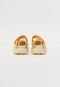 Sandaler med en beige såle, gule og grønne stropper, med justerbar maskinvare og en strukturert bakpanel. Egnet for utendørs bruk.
