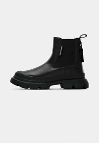Botas de tornozelo pretas com um acabamento em couro liso, painéis laterais elásticos, sola de borracha espessa e uma aba na parte de trás para facilitar o calçar.