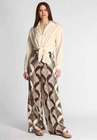 Blusa di crema morbida legata in vita, abbinata a pantaloni a gamba larga con un motivo di foglie di palma marrone e bianco. Tessuto morbido e vestibilità rilassata.