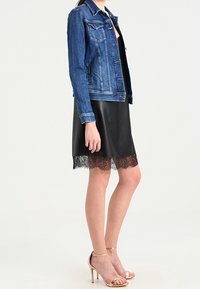 Džínová bunda s klasickým střihem a dvěma předními kapsami, doplněná černými koženými šaty s krajkovým lemem. Celý vzhled doplňují sandály na vysokém podpatku.