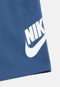 Μπλε αθλητικό σορτς από βαμβακερό μείγμα ύφασμα με μεγάλο λευκό λογότυπο "NIKE" και σχέδιο swoosh στην αριστερή πλευρά.