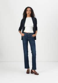 Navy ribbed cardigan over a white fitted top, paired with dark blue straight-leg jeans and brown loafers with gold accents.