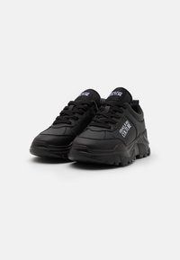 Zapatillas deportivas negras con una parte superior sintética suave, puntera redondeada, suela texturizada y diseño de cordones. Presenta acentos de logo en el costado.