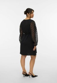 Zwarte jurk met ondoorzichtige bodice en doorschijnende puff mouwen met zwarte stippen. Draag met zwarte slingback hoge hakken.