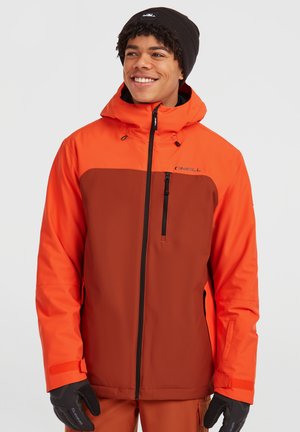 Heren ski-jack in twee tinten, helder oranje en bruin, met een capuchon, ritssluiting aan de voorkant en een borstzak. Handschoenen en een muts maken de look compleet.