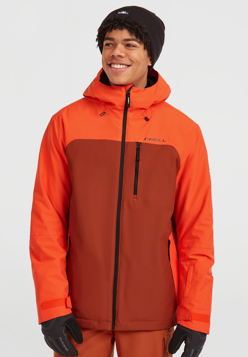 Herre tofarvet skijakke i skarp orange og brun, med hætte, frontlynlås og brystlomme. Vanter og hue fuldender looket.