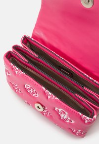 Portefeuille rose avec motifs floraux blancs, ouvert montrant trois compartiments vides et une fermeture par bouton magnétique sur fond blanc.
