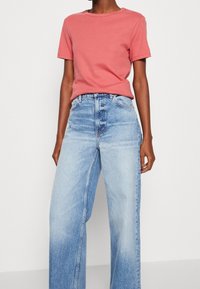 Ljus korallfärgad t-shirt med kort ärm, ihopparad med högmidjade, vida ljusblå jeans. Bomullsmaterial med en slät textur och minimal design.