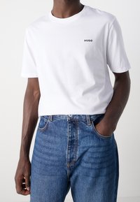 Wit katoenen T-shirt met ronde hals, voorzien van een klein zwart "HUGO" logo op de borst, gecombineerd met blauwe spijkerbroek.