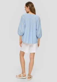 Hellbluse mit Streifen, Puffärmel, lockerer Schnitt und gerafftem Halsausschnitt. Kombiniert mit weißen Leinen-Shorts und beigen Sandalen.