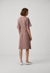 Elastyczna, lawendowa sukienka o luźnym kroju, krótki rękaw, pasek w talii i długość do kolan. Gładka faktura i prosty design.