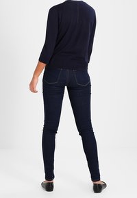Mörkblå stickad tröja med 3/4-ärmar; åtsittande mörkblå jeans; slät yta; smal silhuett; platta svarta skor; minimal detaljering på baksidan.