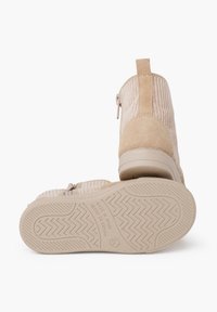 Botines de ante beige con tejido acanalado, cierre de cremallera y suela de goma texturizada, que presenta un sutil patrón de relieve para un mejor agarre.
