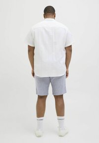 Chemise blanche à manches courtes avec un motif texturé, associée à un short gris clair. Portée avec des baskets blanches et des chaussettes avec logo.