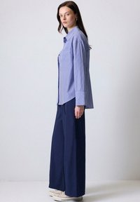 Camisa de rayas azul claro con un corte relajado, diseño de botones, dos bolsillos delanteros, combinada con pantalones de pierna ancha en color marino y zapatillas blancas.