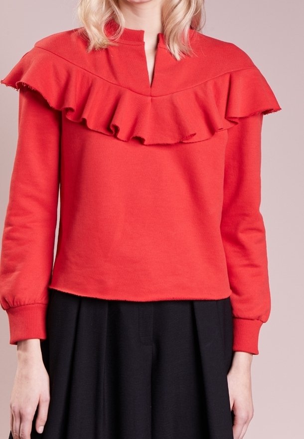 Sweat-shirt rouge en coton avec un col à volants, manches longues et coupe décontractée, associé à une jupe noire. Texture douce et design décontracté.