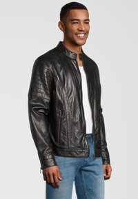 Zwarte leren motorjack met een opstaande kraag, ribbeldetails op de schouders en ritszakken. Draag het over een wit shirt en blauwe jeans.