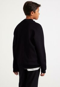 Schwarzer Pullover mit geripptem Kragen und Bündchen, von hinten gezeigt. Aus weichem Stoff gefertigt, mit langen Ärmeln und lässiger Passform.