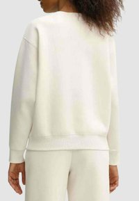 Felpa color crema con vestibilità rilassata, polsini e orlo a costine. Tessuto morbido con una texture liscia, senza motivi o dettagli visibili.