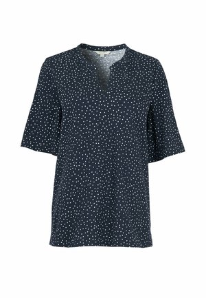 Marineblaue Bluse mit weißen Punkten, kurzen Ärmeln und einem leichten V-Ausschnitt vor schlichtem Hintergrund.