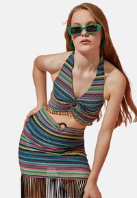 Kolorowy, paskowany halter top z węzłem z przodu i koralikowymi akcentami, połączony z dopasowaną spódnicą z frędzlami, obie z miękkiej, teksturowanej tkaniny.