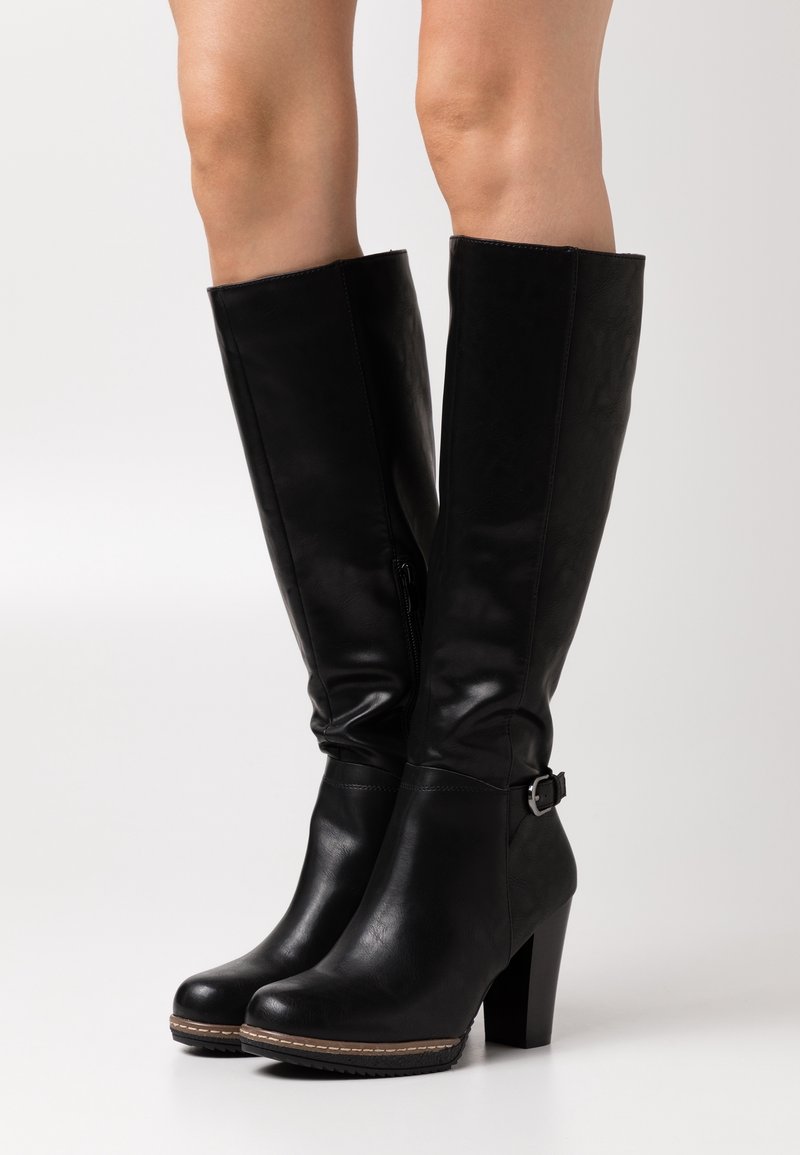 Bottes en cuir noires montant jusqu'aux genoux avec talons épais et détail de boucle latérale, portées sur jambes nues sur un fond uni.