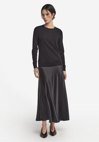 Sort langærmet sweater lavet af blødt stof, kombineret med en sort satin maxi-nederdel med et glat, flydende design og sorte spidse hæle.