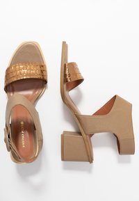 Beige nahka sandaalit, joissa on teksturoitu kultainen yksityiskohta, avonainen kärki ja muotoiltu lohkoheels. Varustettu säädettävällä nilkkahihnalla.