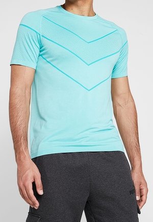 Hombre con camiseta deportiva azul claro de manga corta con estampados de espiga texturizados y pantalones deportivos Puma gris oscuro.